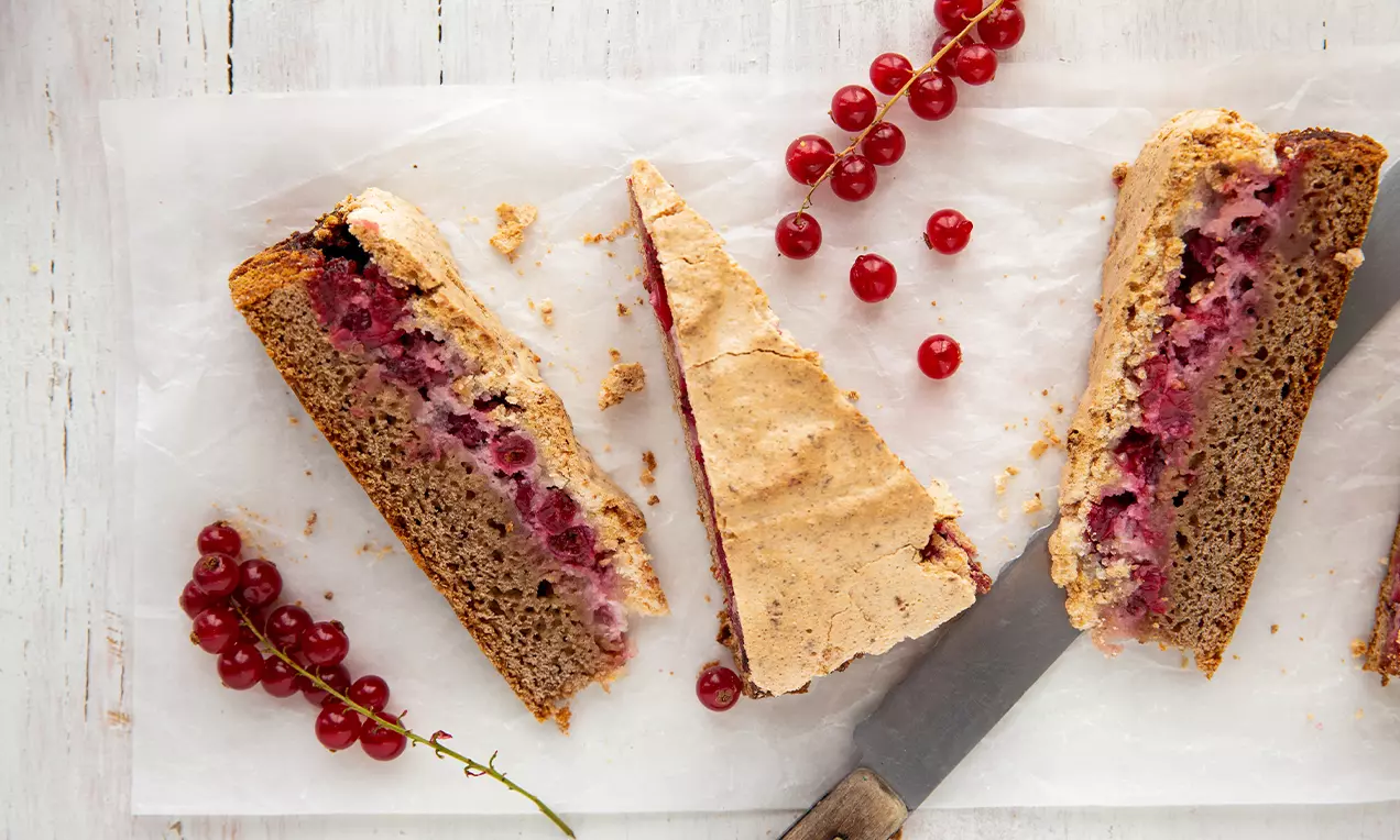 Tranches triangulaires de gâteau doré avec une couche de groseilles rouges juteuses et une croûte légèrement craquelée sur du papier blanc