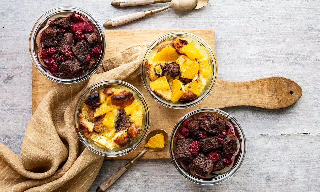 Im Glas geschichteter süßer Gratin mit goldgelber Creme und knusprigen Bröseln, garniert mit fruchtigen Himbeeren und Orangenscheiben