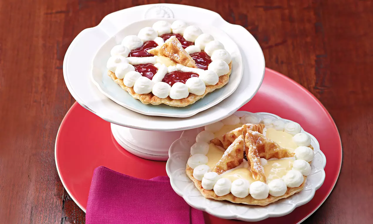 Tartelette ronde en pâte feuilletée garnie de crème blanche et de confiture rouge, décorée de triangles dorés sur des assiettes colorées