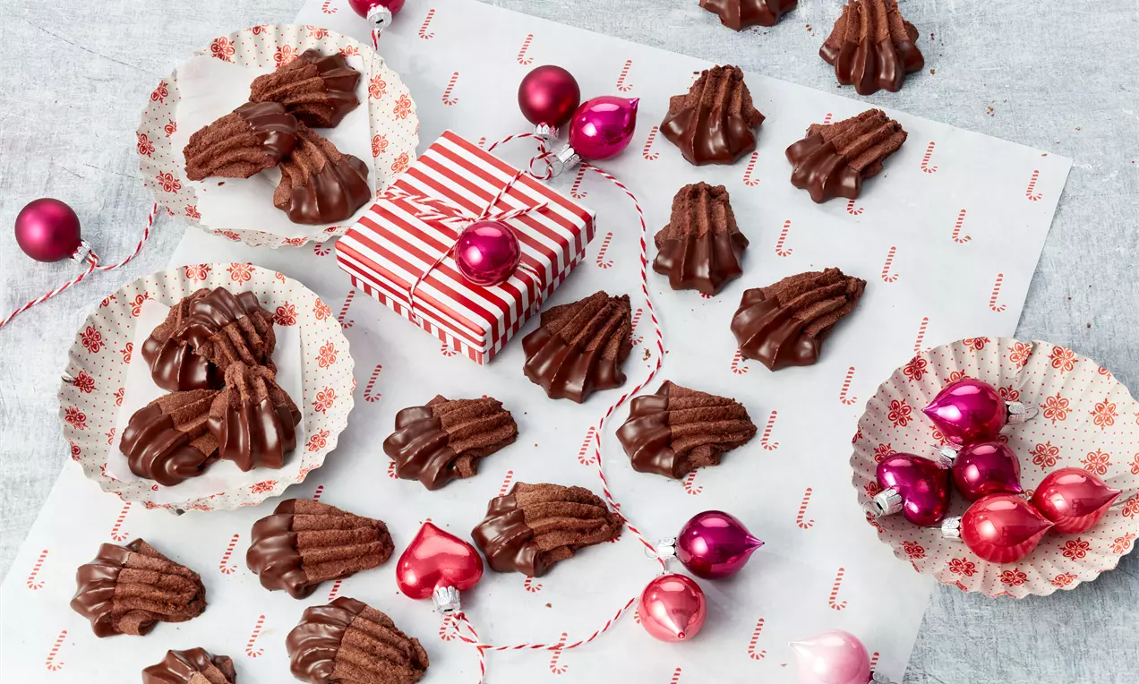 Schokoladenbraune Bärentatzen mit geriffelter Textur auf weihnachtlichem Papier umgeben von roten Christbaumkugeln und Geschenkpaketen