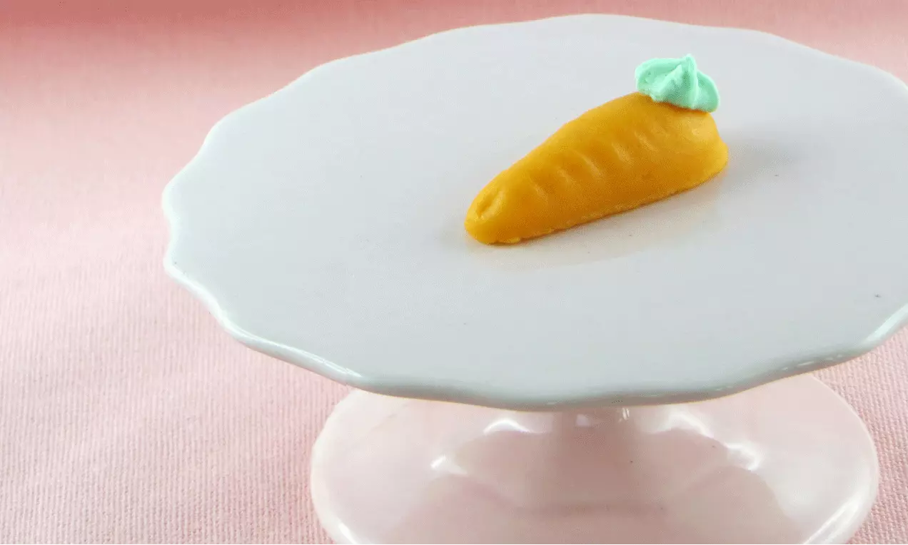 Orangenfarbene Marzipan-Karotte mit feinen Einkerbungen und grüner Blattverzierung auf einer weißen, schlichten Tortenplatte