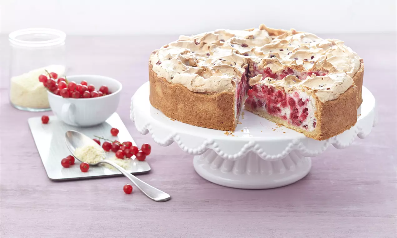 Runde Johannisbeer-Baiser-Torte mit goldbraunem Mürbeteigboden, heller Baiserdecke und roten Beerenfüllung auf weißer Tortenplatte