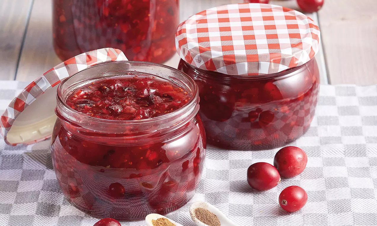 Confiture aux fruits rouges brillants dans des pots en verre à couvercles à carreaux blancs et rouges, posés sur un tissu à motif vichy