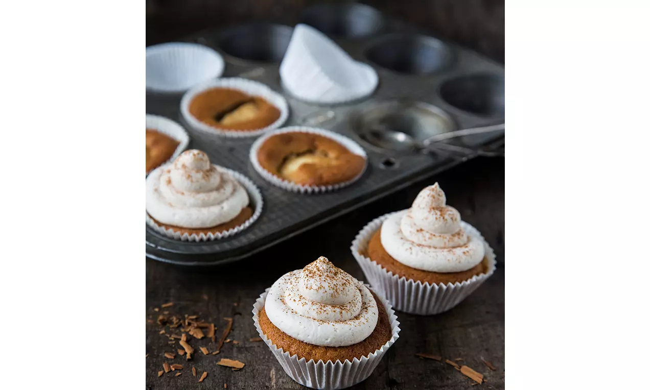 Cupcakes dorés à la pomme en caissettes blanches avec une spirale de crème saupoudrée de cannelle sur un fond rustique