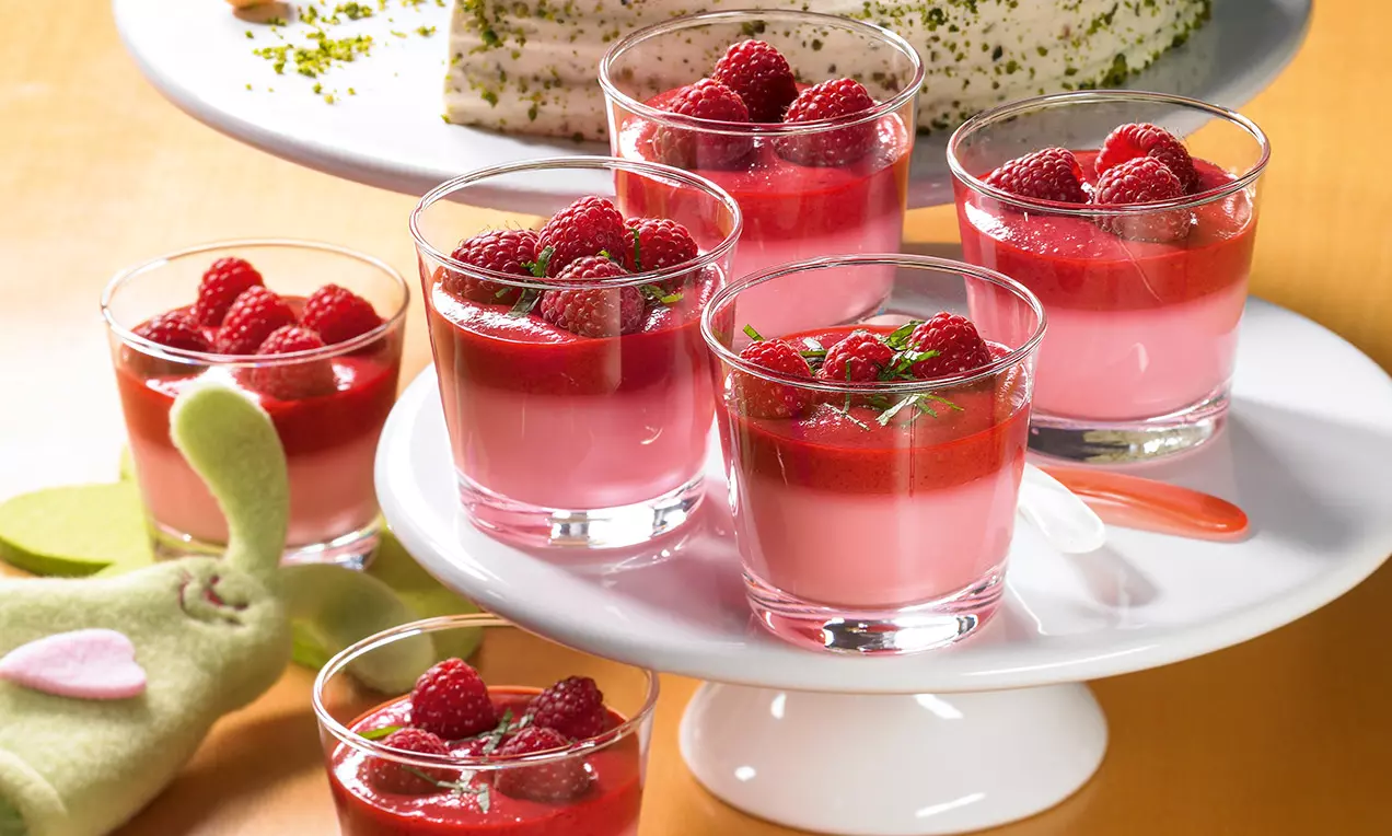 Verrines roses à la mousse framboise garnies de coulis rouge vif, framboises brillantes et feuilles de menthe sur un plateau blanc