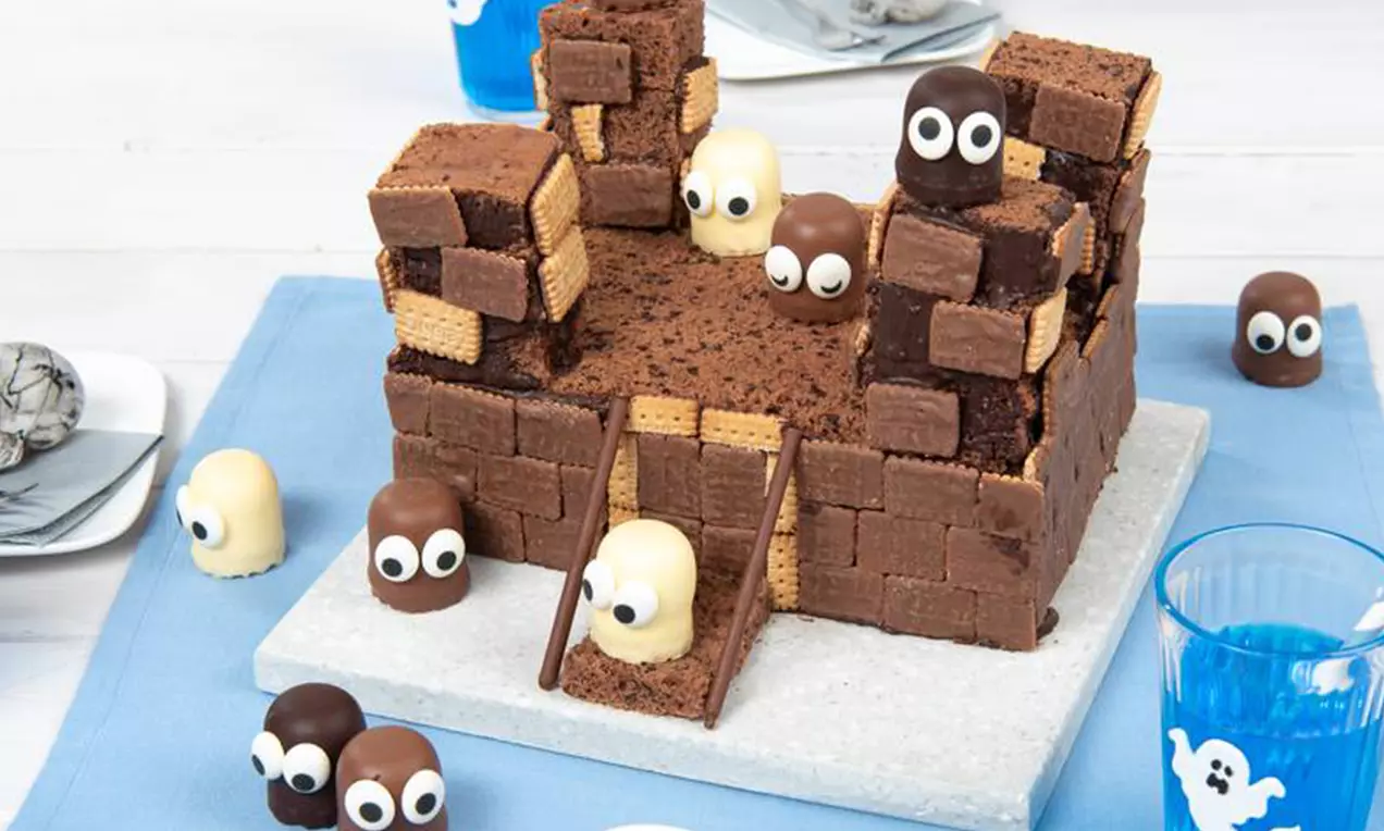 Château en morceaux de gâteau au chocolat sombre et de biscuits dorés, garni de fantômes en chocolat blanc et au lait avec des yeux