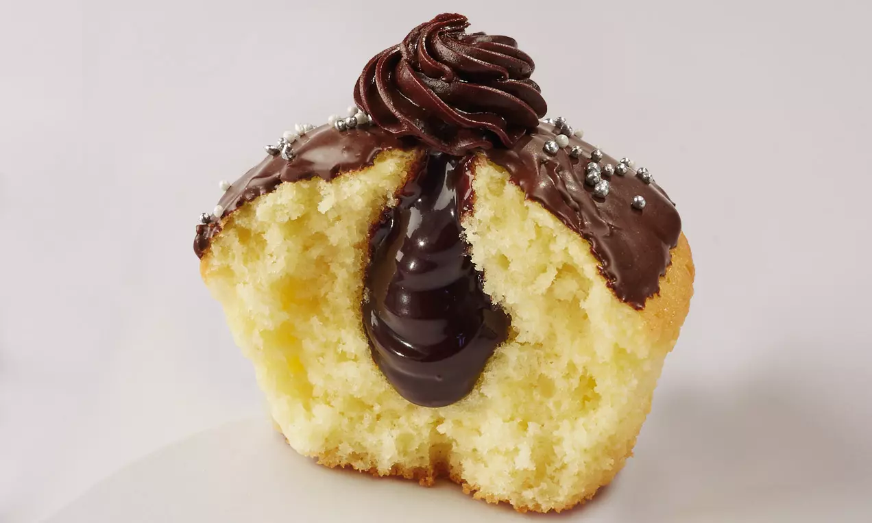 Cupcake soffice color dorato con cuore liquido di cioccolato scuro, glassa lucida e decorazioni argentate su un piatto bianco