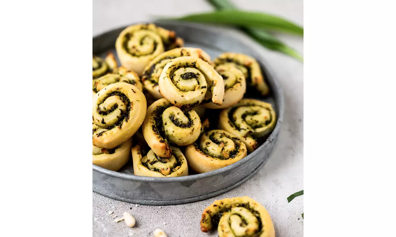 Escargots dorés enroulés en spirale garnis d’ail des ours vert vif sur un plateau rond en métal posé sur une surface claire