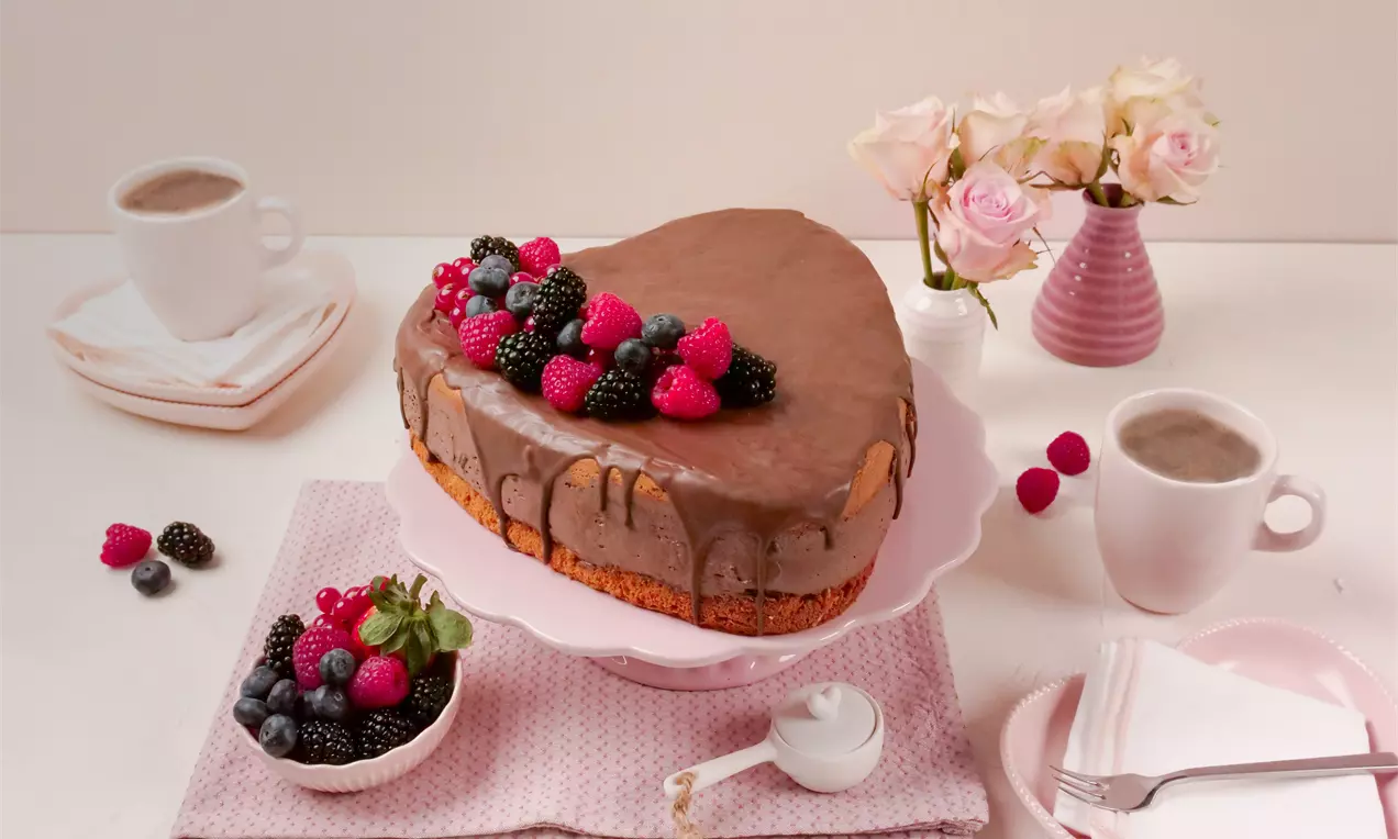 Gâteau en forme de cœur recouvert d’un glaçage au chocolat brillant, garni de fruits rouges et noirs sur un plat rose