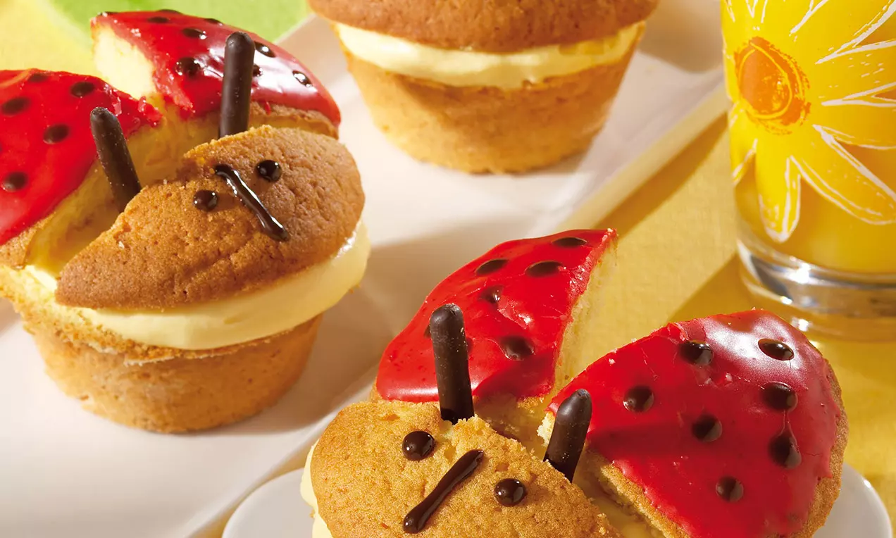 Cupcake dorati con ripieno di crema chiara, decorati con ali di glassa rossa punteggiata di nero e antenne di cioccolato su un vassoio