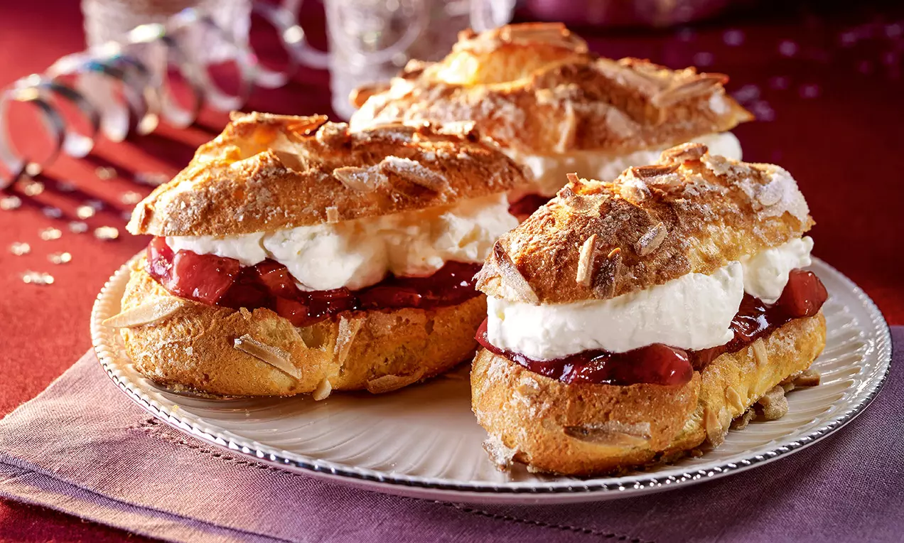 Éclairs dorés garnis d'une crème blanche aérienne et d'une compotée de prune rouge brillante, parsemés d'amandes sur une assiette blanche