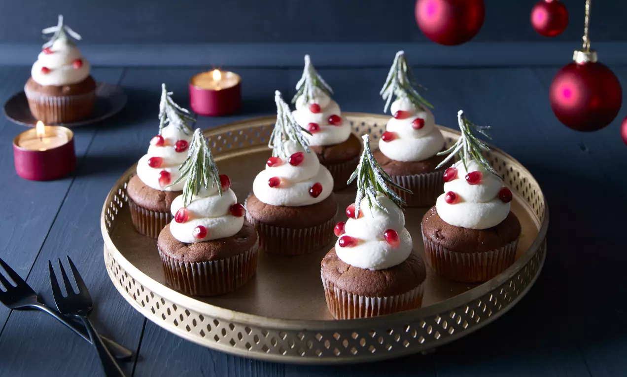 Schokoladen-Cupcakes mit weißer Sahnehaube, roten Granatapfelkernen und Rosmarinzweigen auf goldenem Servierteller, festlich dekoriert