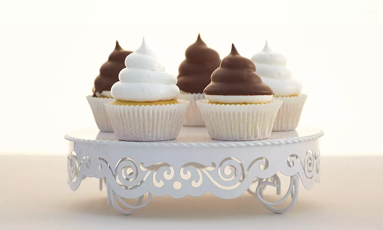 Cupcake soffici con copertura a spirale di meringa bianca e cioccolato lucido, disposti su un elegante alzata bianca decorata