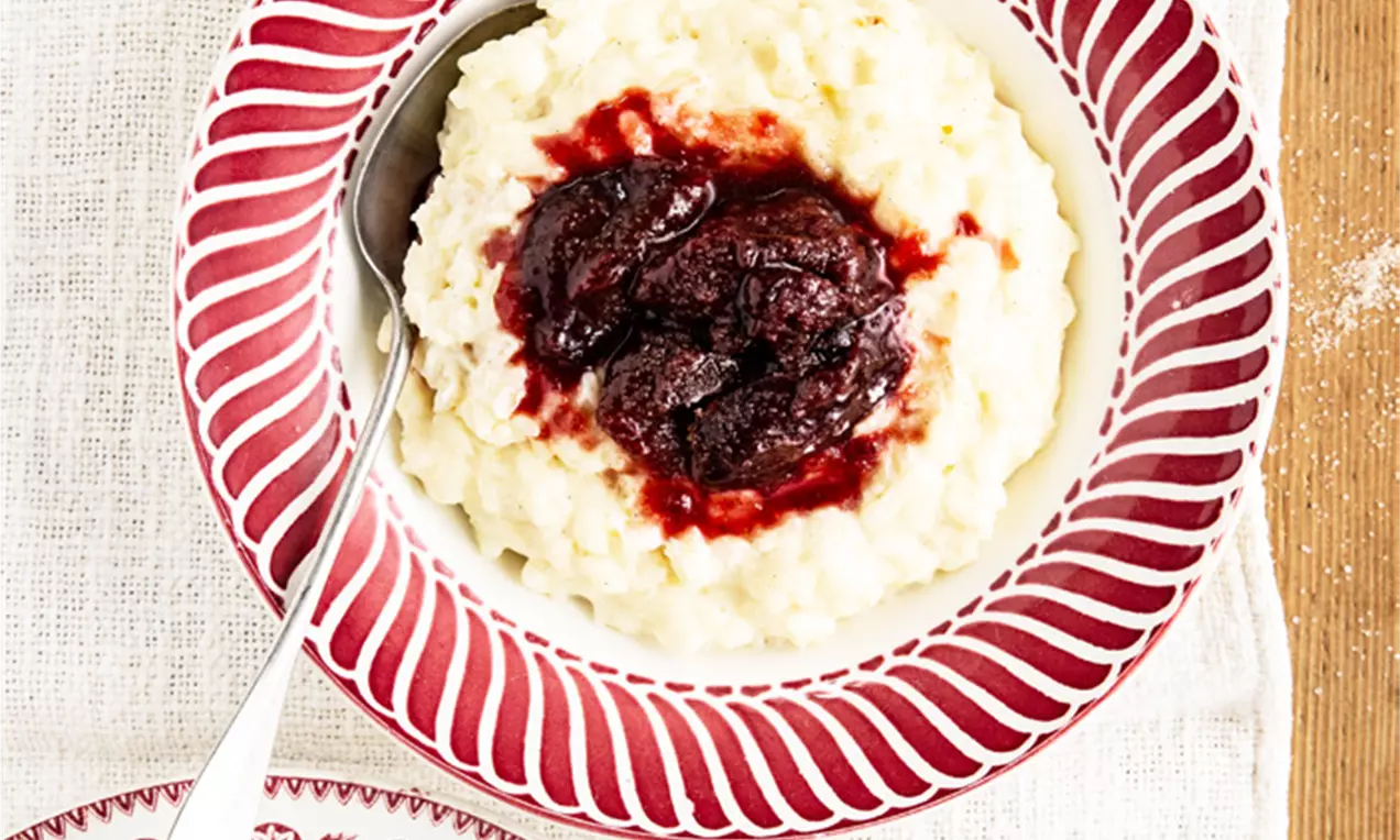 Riz au lait crémeux blanc garni de compote rouge brillante, présenté dans une assiette à motifs rouges sur une nappe claire