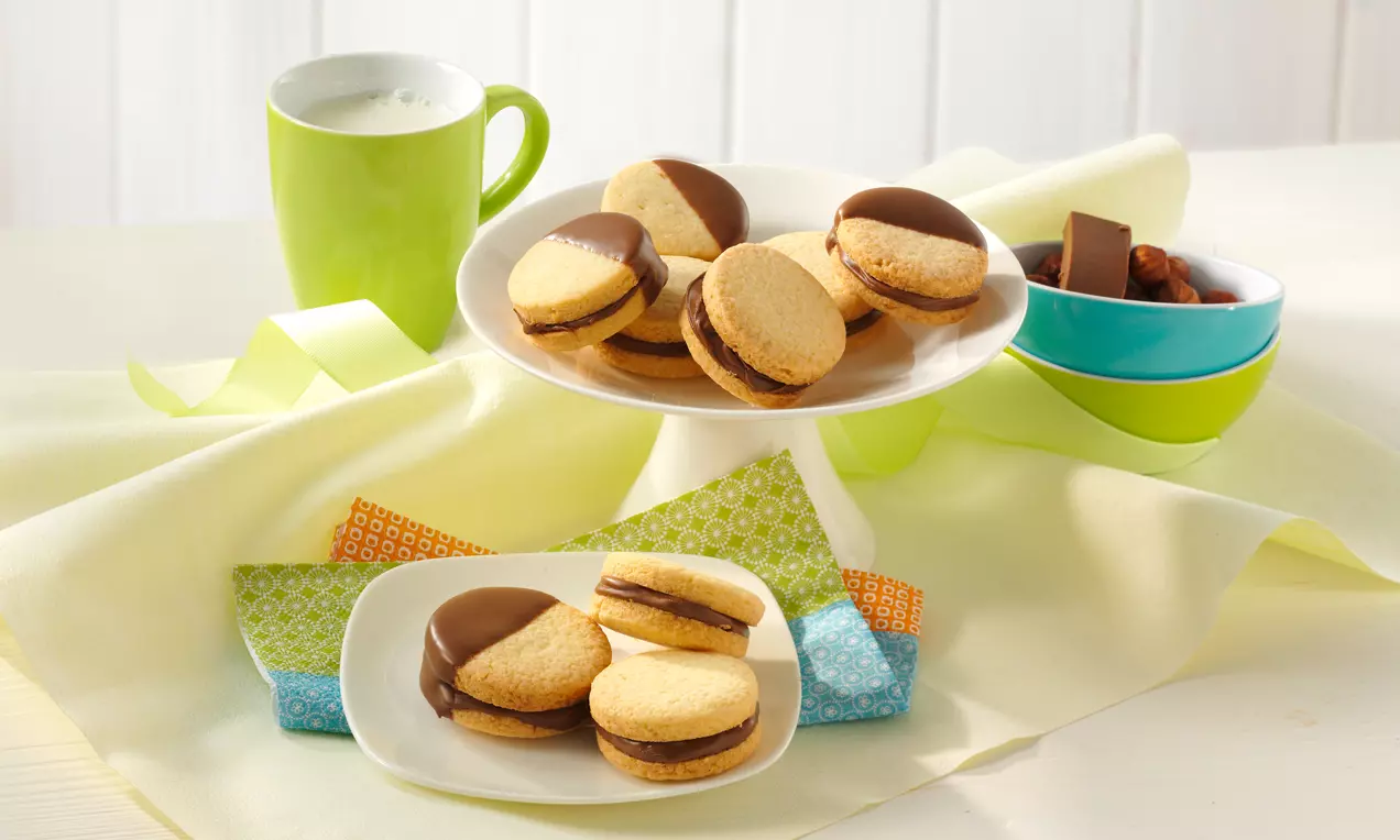 Biscuits ronds dorés fourrés de crème au nougat, moitié recouverts de chocolat brillant, disposés sur des assiettes blanches