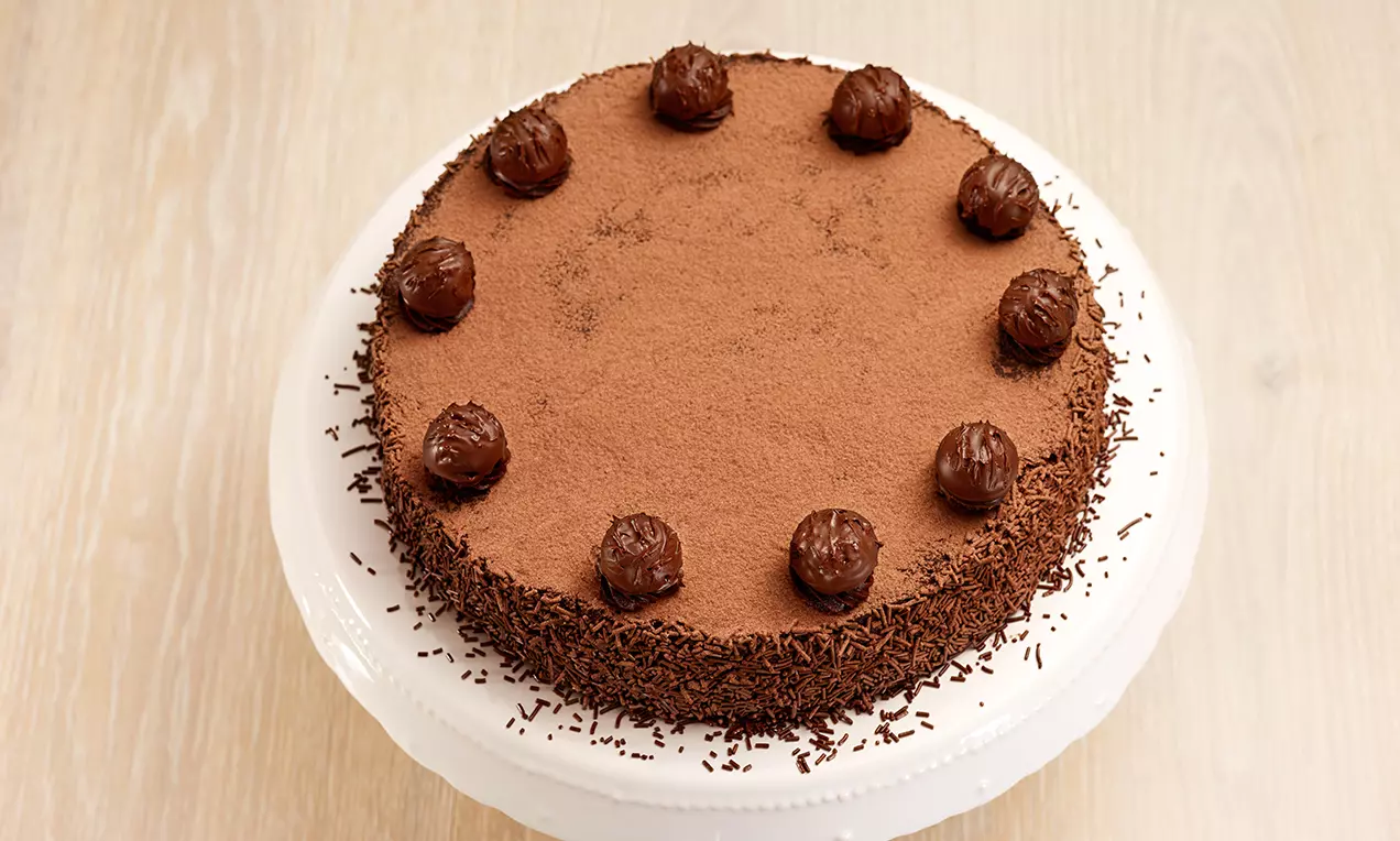 Tarte ronde au chocolat garnie de truffes marron foncé disposées en cercle, surmontée de cacao et entourée de vermicelles chocolatés