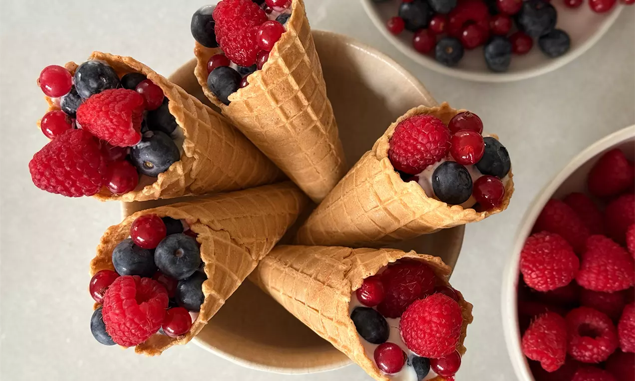 Knusprige Waffelhörnchen gefüllt mit frischen roten Himbeeren, glänzenden Johannisbeeren und tiefblauen Heidelbeeren in einer Keramikschale