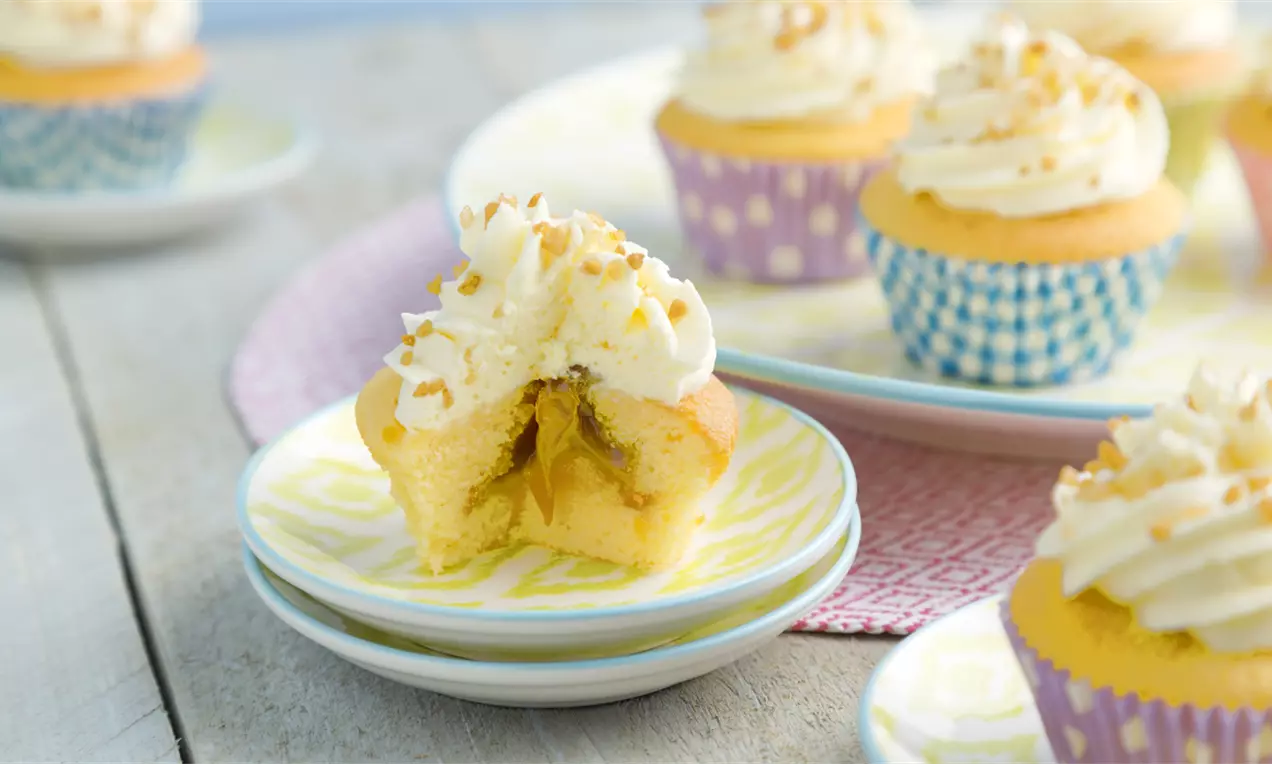 Cupcakes moelleux dorés en caissettes colorées, garnis de crème blanche et de pralines avec un cœur fondant à la citronnée sur des assiettes pastel