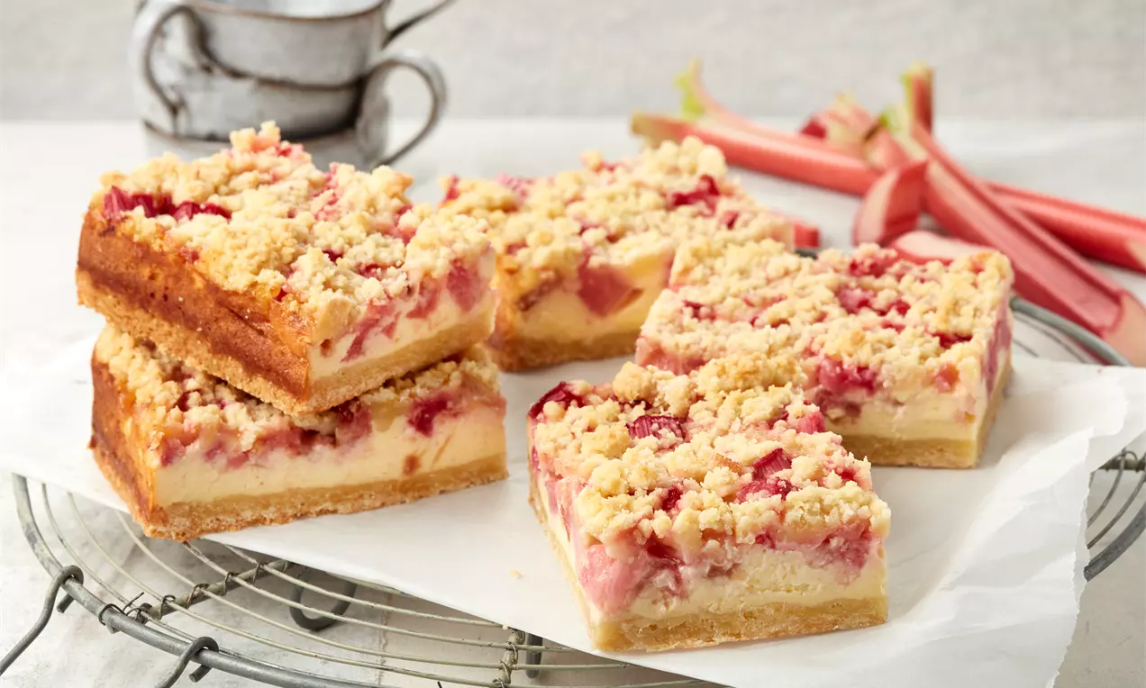 Rhabarber-Quarkkuchen mit goldbrauner Streuselkruste, rosa Rhabarberstücken und heller Quarkfüllung auf Backpapier auf einem Gitter