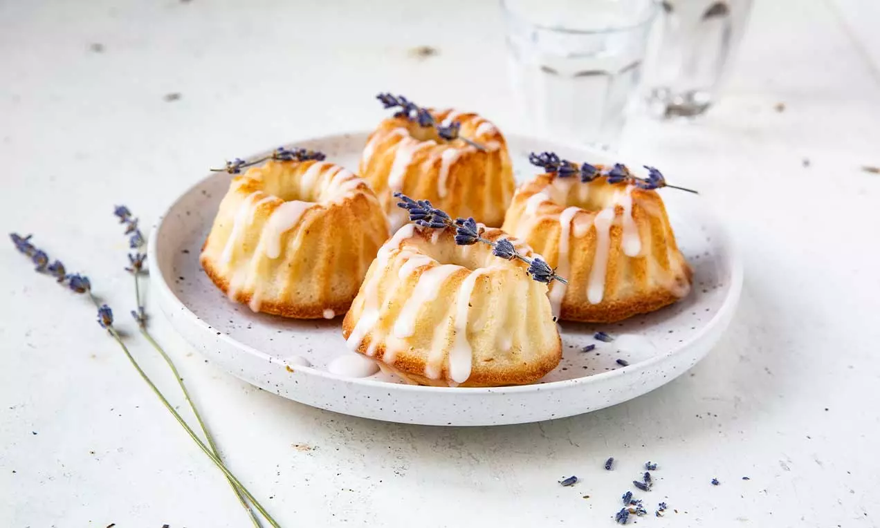 Petits gâteaux dorés en forme de couronnes, glacés de blanc et décorés de brins de lavande sur une assiette blanche rustique
