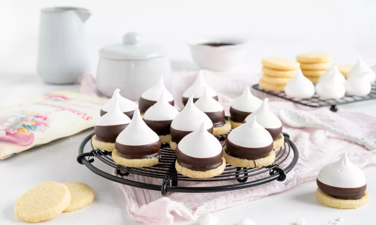 Cookies au chocolat et à la meringue brillants et bombés sur une base dorée, disposés sur une grille noir mat avec une nappe rose