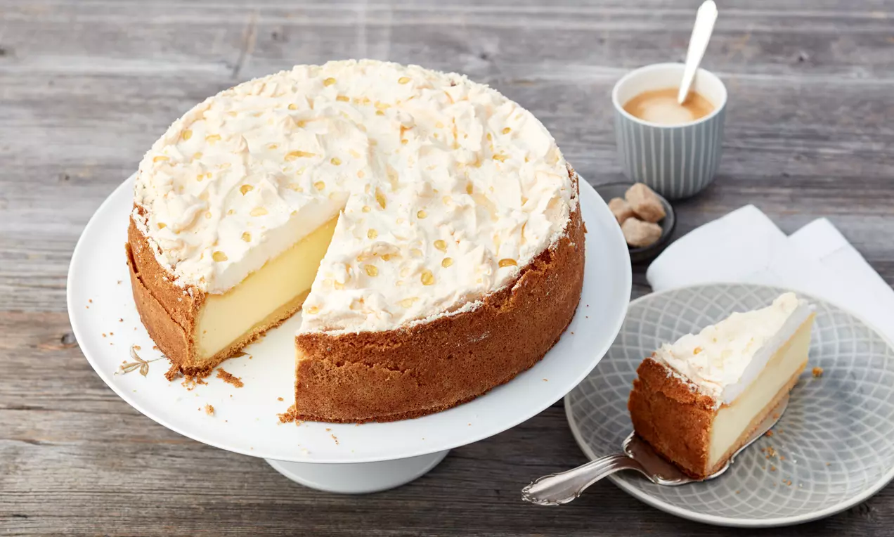 Goldtröpfchen-Torte mit goldbraunem Mürbeteigrand, heller Quarkfüllung und luftiger Baiserhaube mit goldenen Tröpfchen auf weißer Kuchenplatte