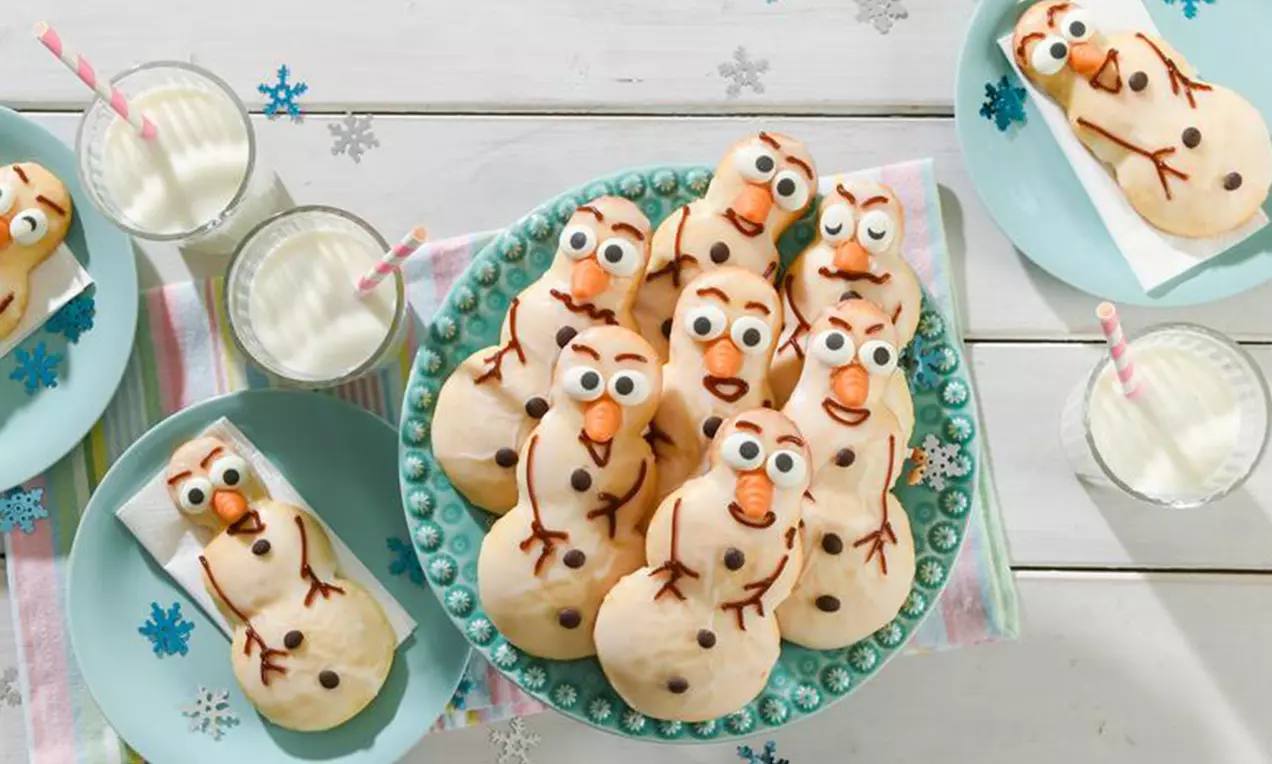 Goldbraune Schneemann-Plätzchen mit schokoladigen Details und bunter Verzierung auf einem türkisfarbenen Teller mit buntem Stoff drapiert