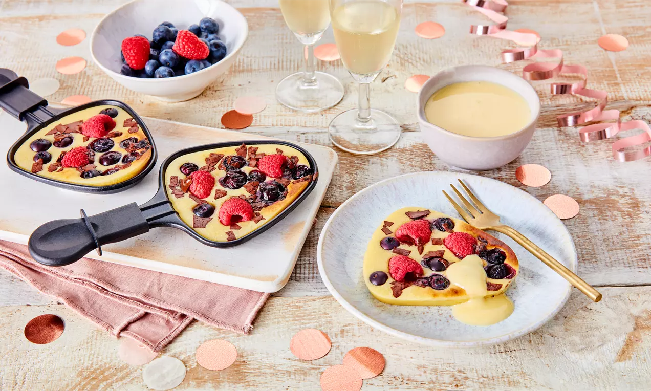 Geschmolzene gelbe Crème mit frischen roten Himbeeren und dunklen Blaubeeren, serviert in Pfännchen und auf einem Teller mit goldener Gabel