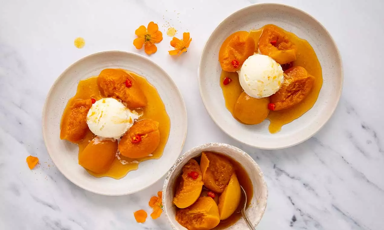Compote de nectarines dorées aux contours doux baignée dans un sirop ambré, servie avec une boule de glace et des éclats rouges
