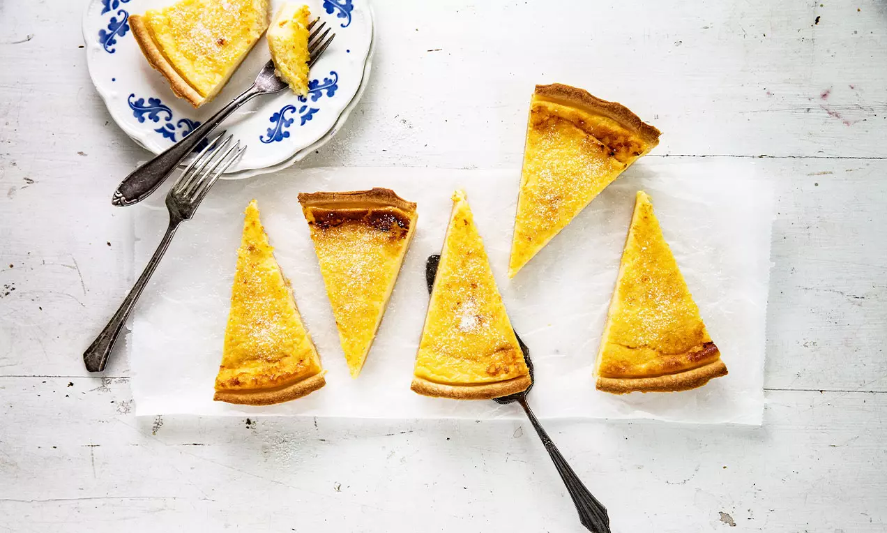 Tranches dorées de gâteau à la crème sur papier blanc, quelques fourchettes argentées et une assiette fleurie en porcelaine