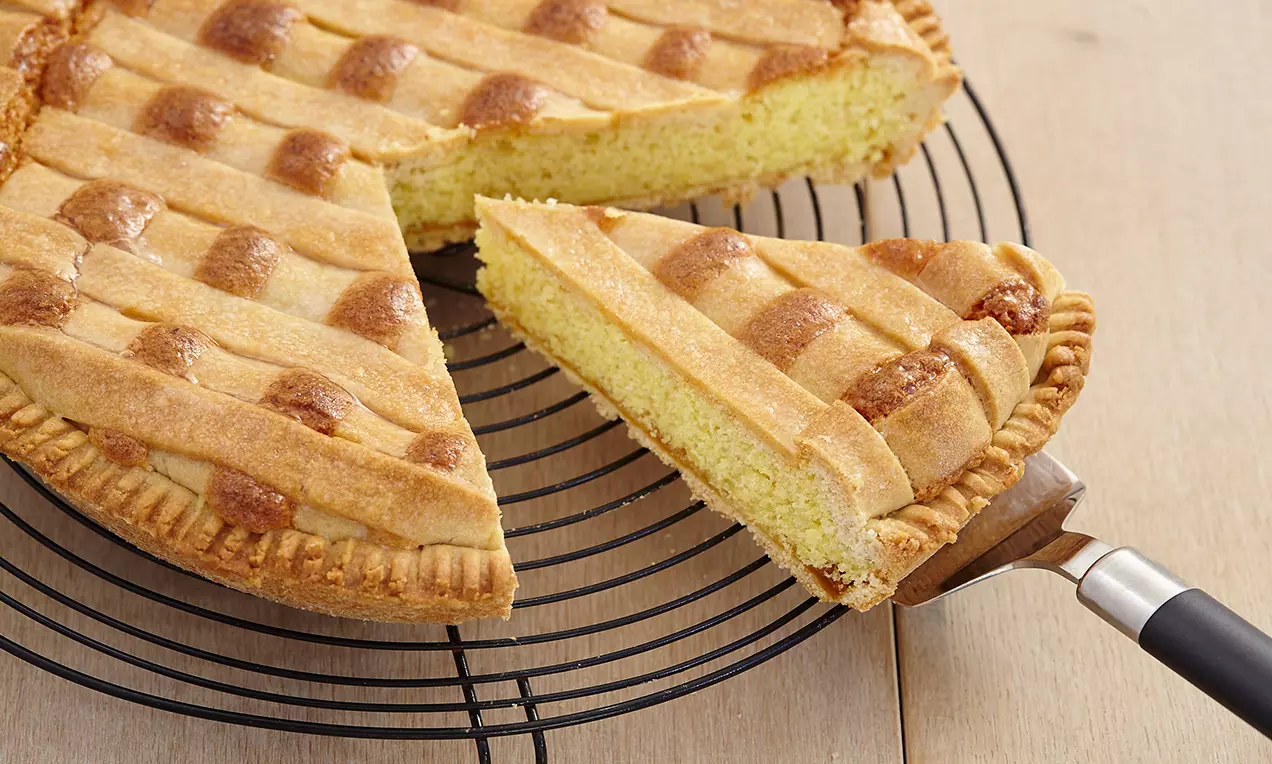 Crostata dorata con intreccio a griglia sopra soffice ripieno giallo chiaro, base bordata e trama zuccherina su una griglia nera