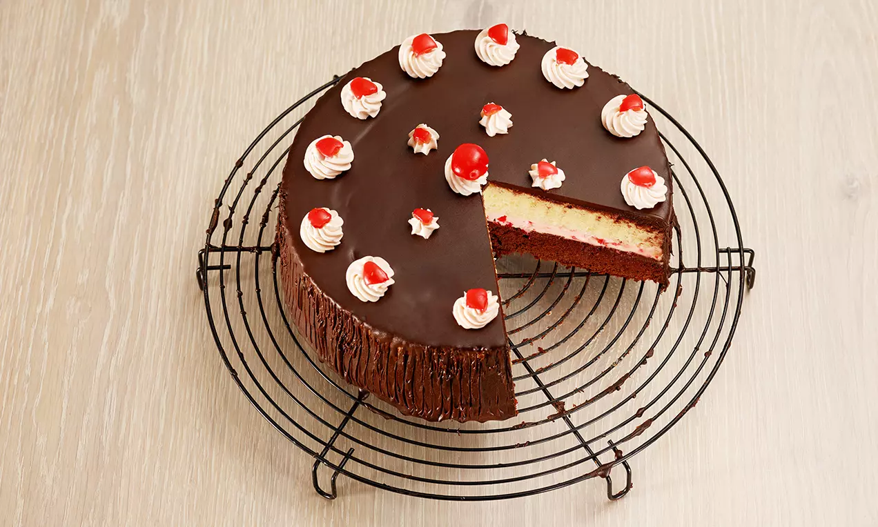 Gâteau rond sur une grille avec glaçage chocolat brillant, décoré de crème blanche et cerises rouges sur un biscuit bicolore