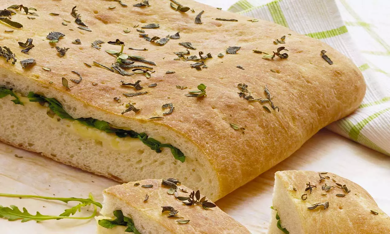 Focaccia dorata e morbida ripiena di formaggio fuso e rucola fresca, con superficie lievemente croccante e cosparsa di erbe aromatiche