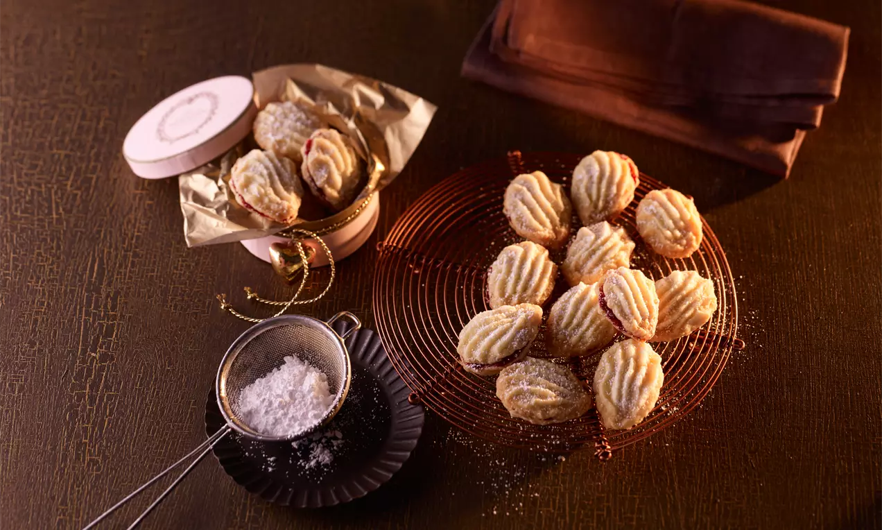 Petits biscuits striés dorés et poudrés de sucre, disposés sur une grille métallique ronde avec un tamis rempli de sucre et une boîte ouverte
