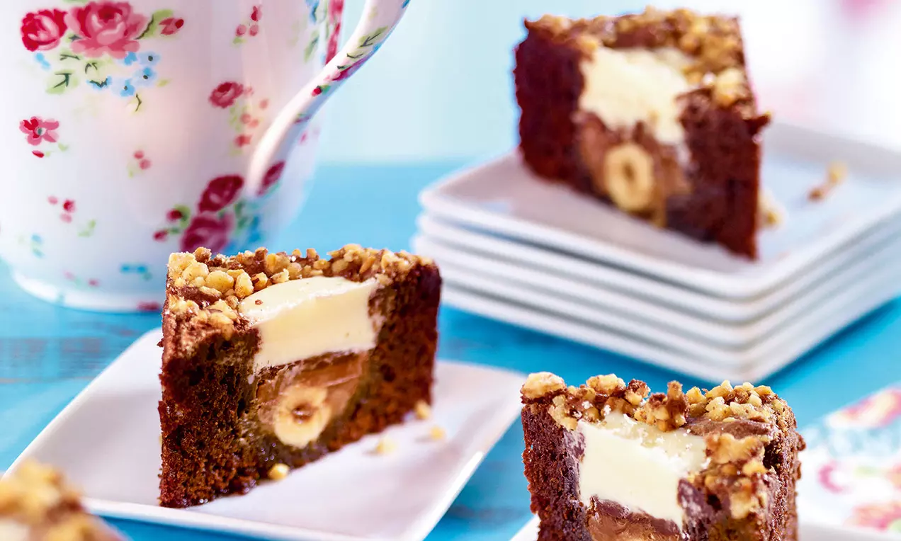 Brownies chocolatés aux coins croquants, avec une couche de crème claire et des noisettes entières, présentés sur des assiettes blanches empilées
