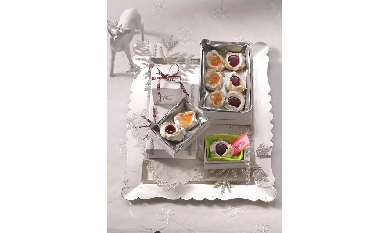 Petits pavlovas ronds et blancs garnis de fruits brillants orange, jaune et violet dans des boîtes argentées sur un plateau festif.
