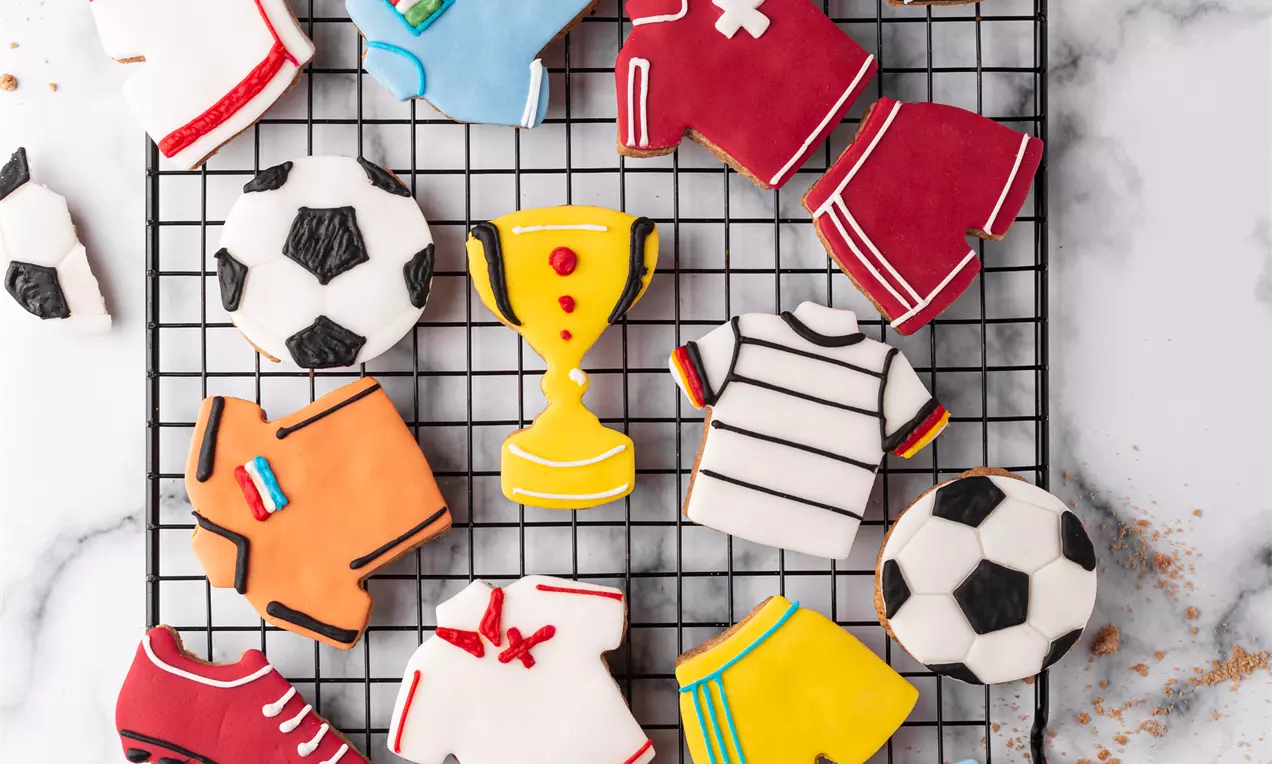 Biscuits colorés en forme de maillots de football, shorts, ballons et trophées, décorés de glaçage sur une grille noire