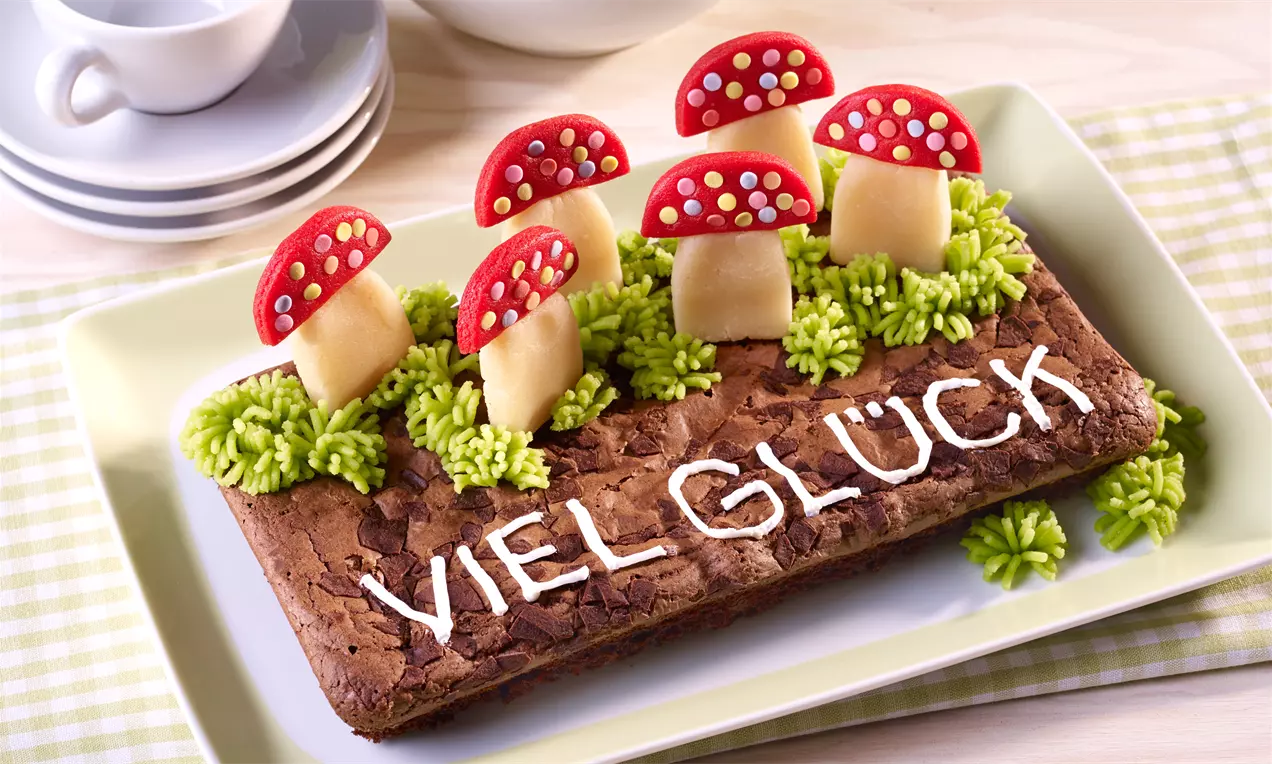 Brownies marron foncé en rectangle décorés de champignons rouges en pâte d'amande, herbe verte en glaçage et inscription blanche