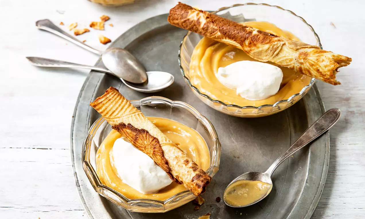 Gebrochen goldene Bretzeli auf hellbrauner, cremiger Brönnti Crème, serviert in Glasdessertschalen auf silbernem Tablett mit Löffeln
