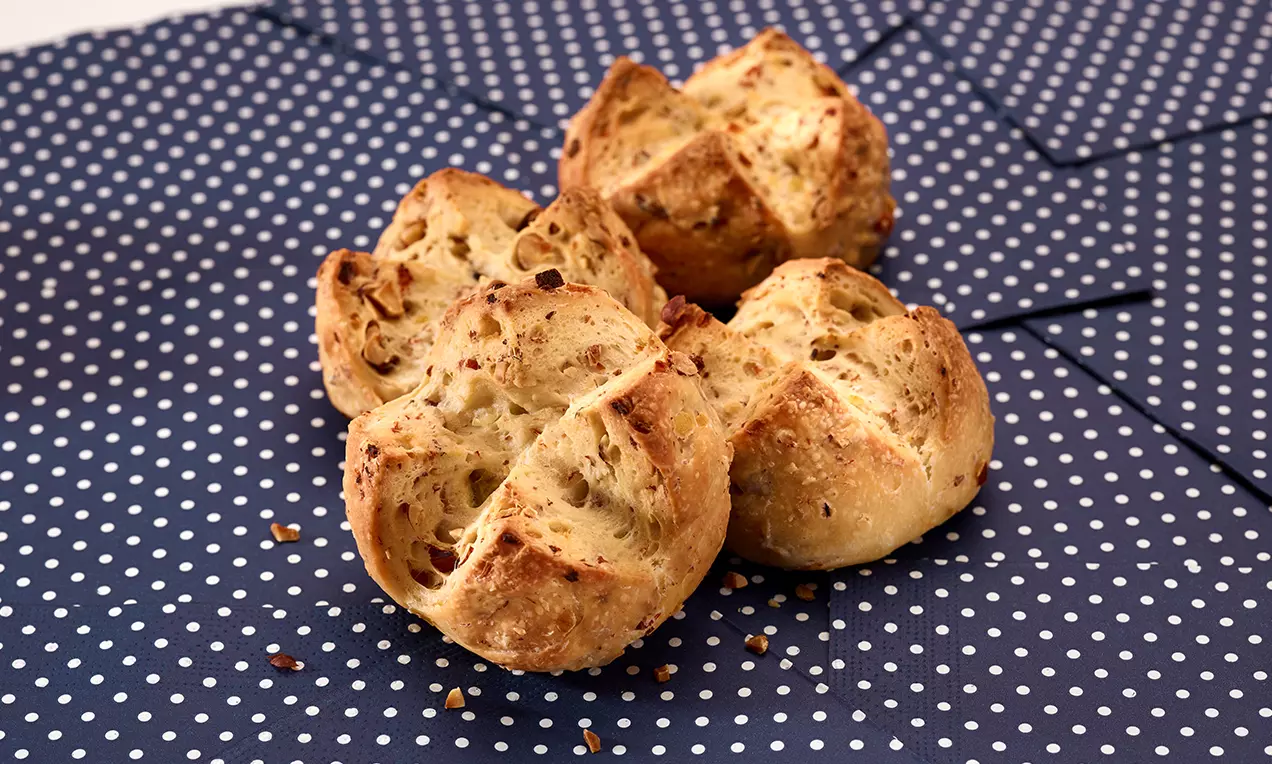 Panini dorati con crosta croccante e spaccature irregolari, disposti su un fondo blu a pois bianchi, con granella sparsa