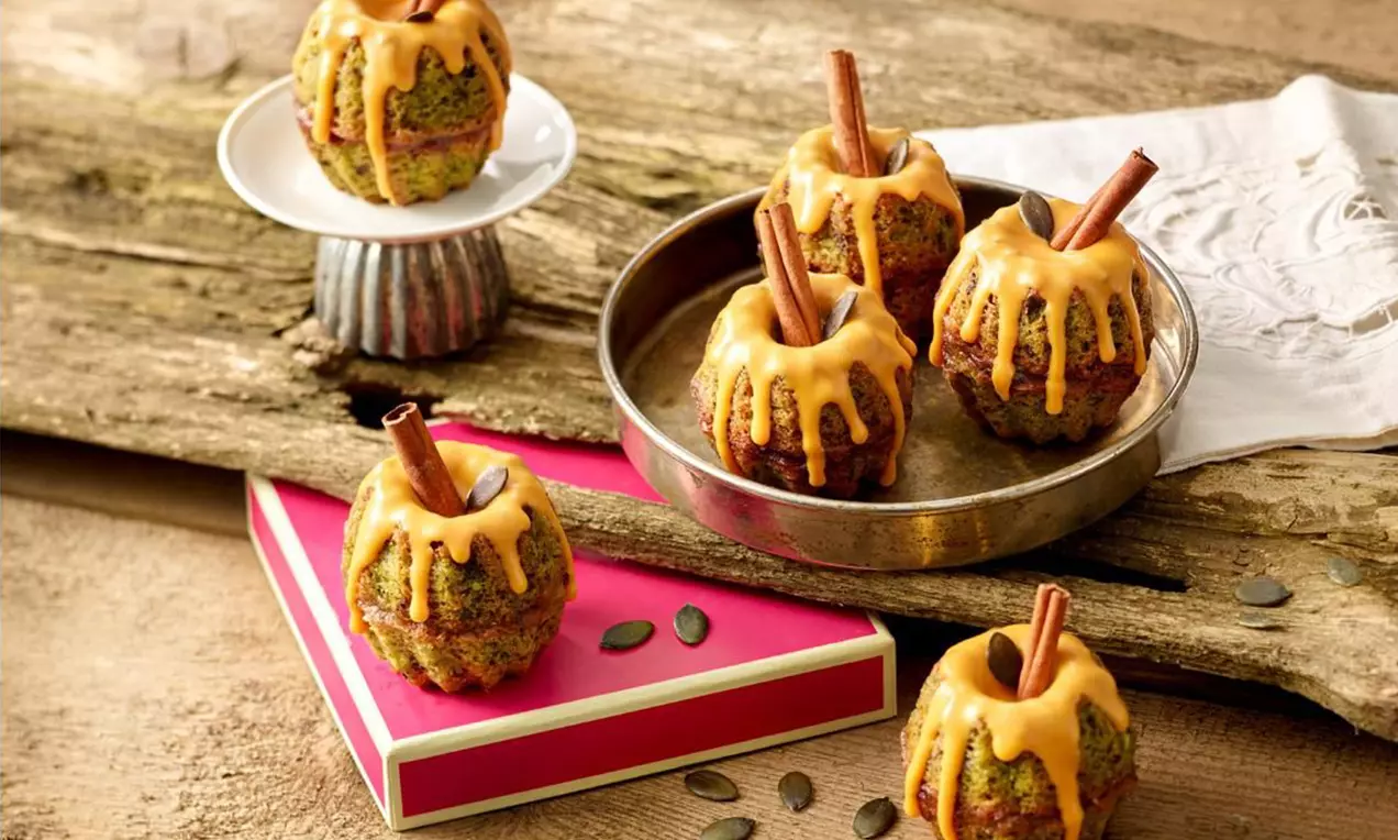 Mini bundt moelleux marbrés vert et brun avec glaçage orange vif coulant, garnis de bâtons de cannelle et disposés sur bois et assiettes