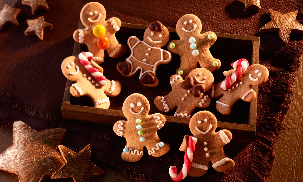 Petits bonhommes Lebkuchen brun doré décorés de glaçage coloré et de sucre, disposés dans une boîte bois sur une nappe marron avec des étoiles
