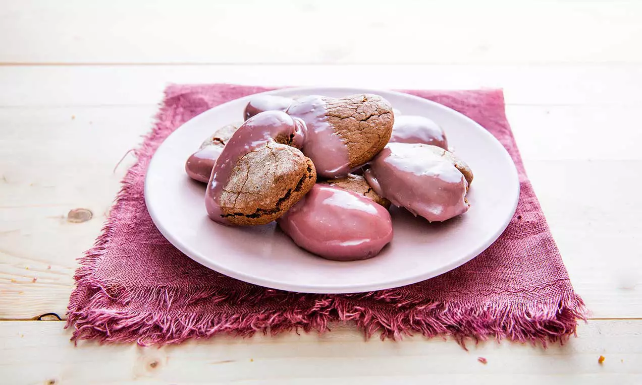 Biscuits en forme de cœur dorés avec un glaçage rose brillant disposés sur une assiette blanche posée sur un tissu rose froissé