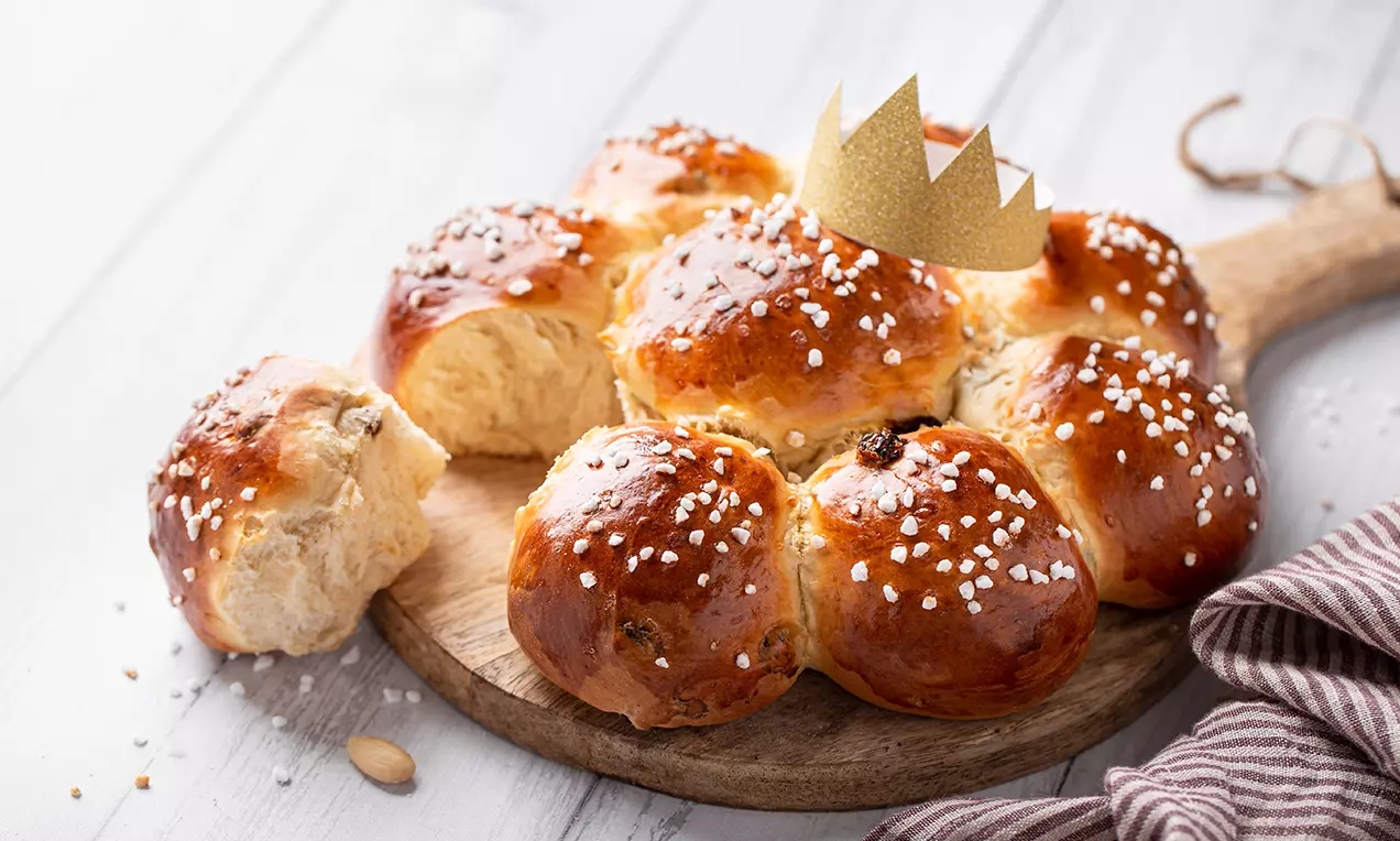 Goldbrauner Dreikönigskuchen aus fluffigem Hefeteig mit glänzender Oberfläche und karamellisierten Zuckerstückchen auf rundem Holzbrett