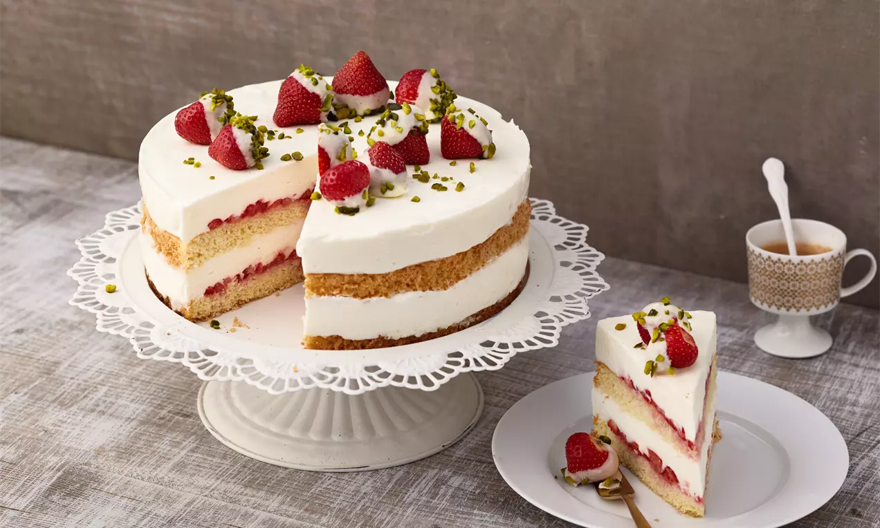 Gâteau à étages avec crème blanche, fraises rouges entières et éclats de pistache sur un présentoir blanc ajouré
