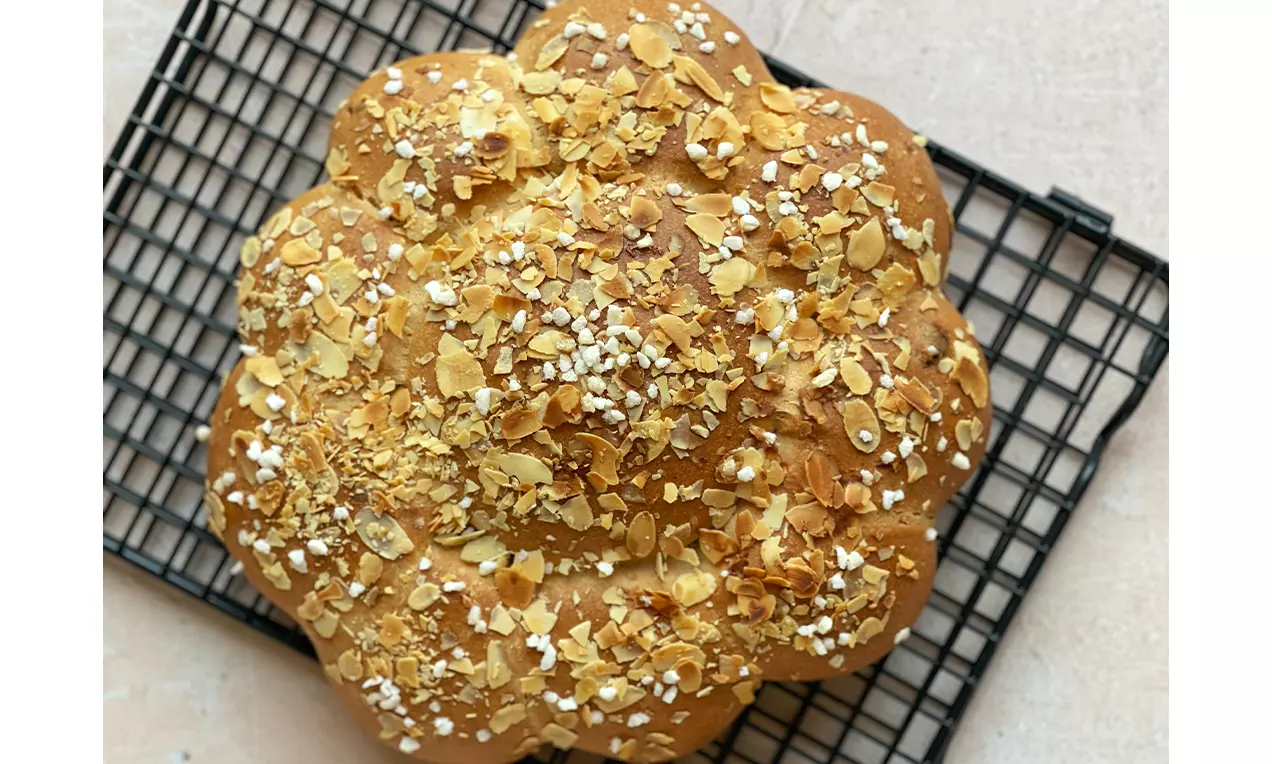 Pane dolce dorato a forma di fiore, arricchito con fiocchi di mandorle croccanti e granella di zucchero su una griglia nera