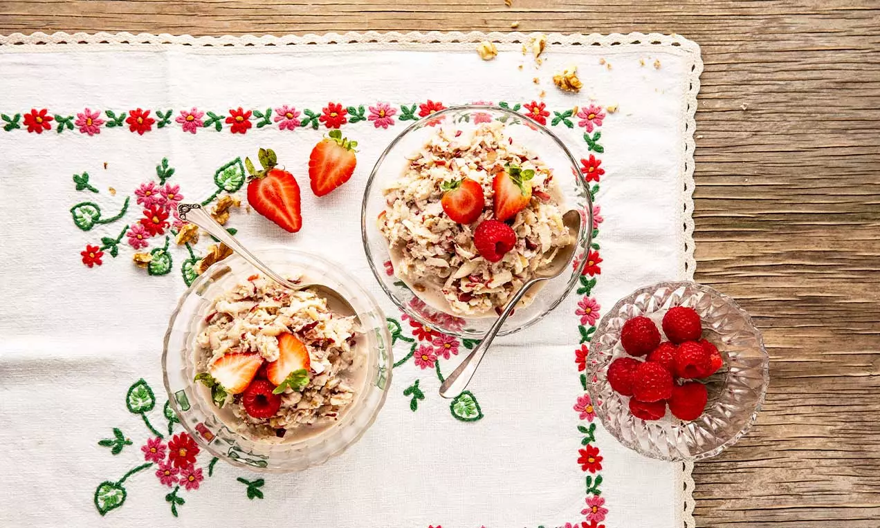 Birchermüesli aux teintes crème parsemé de fruits rouges frais, présenté dans des coupes en verre sur une nappe brodée florale