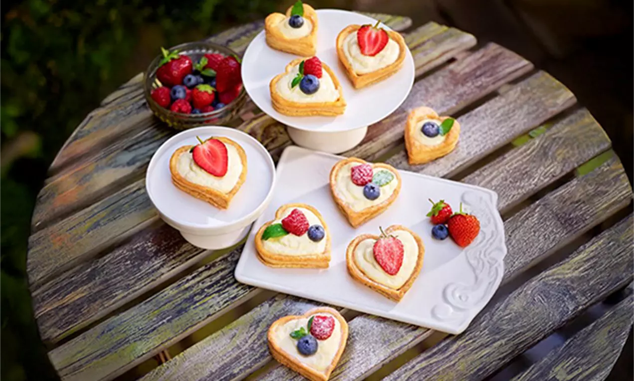 Cœurs dorés en pâte feuilletée croustillante garnis de crème claire et de fruits rouges frais sur une table en bois rustique