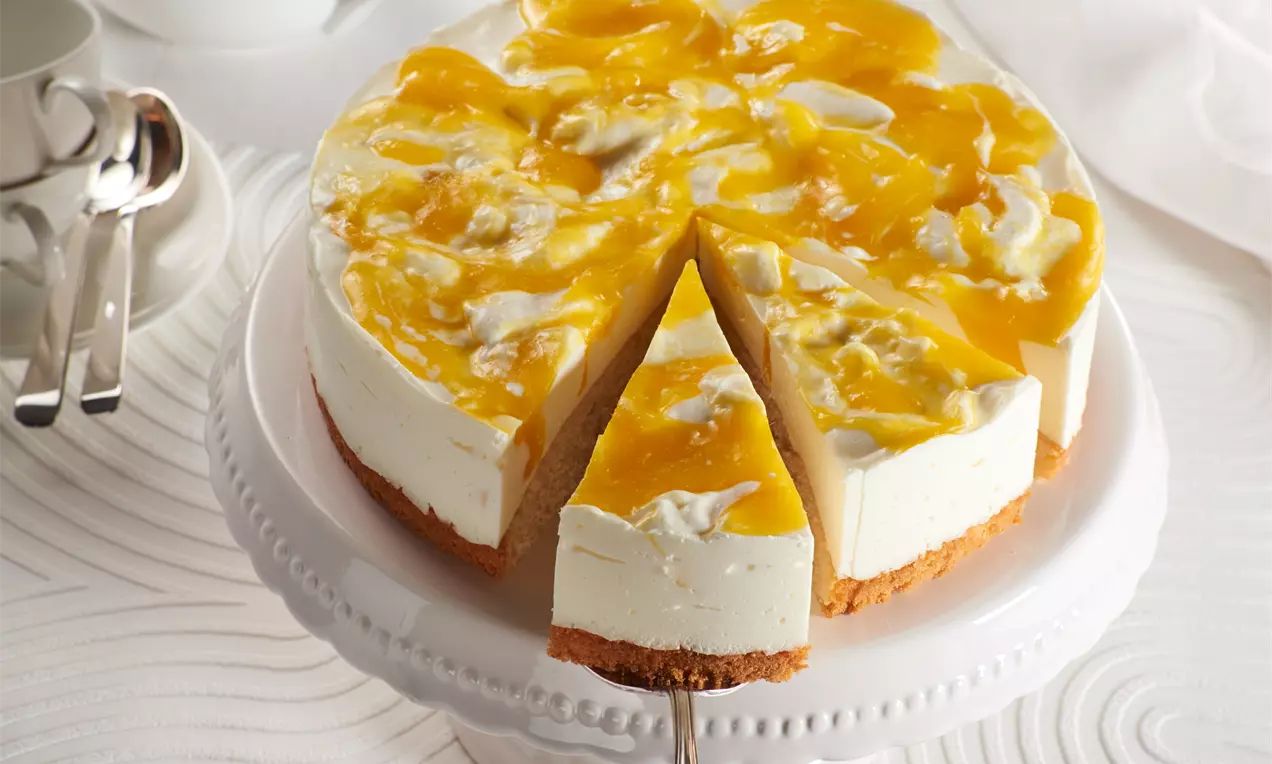 Käse-Rahm-Mango-Torte mit weißer cremiger Füllung auf goldenem Keksboden und leuchtendem, gelb-weiß marmoriertem Mangospiegel