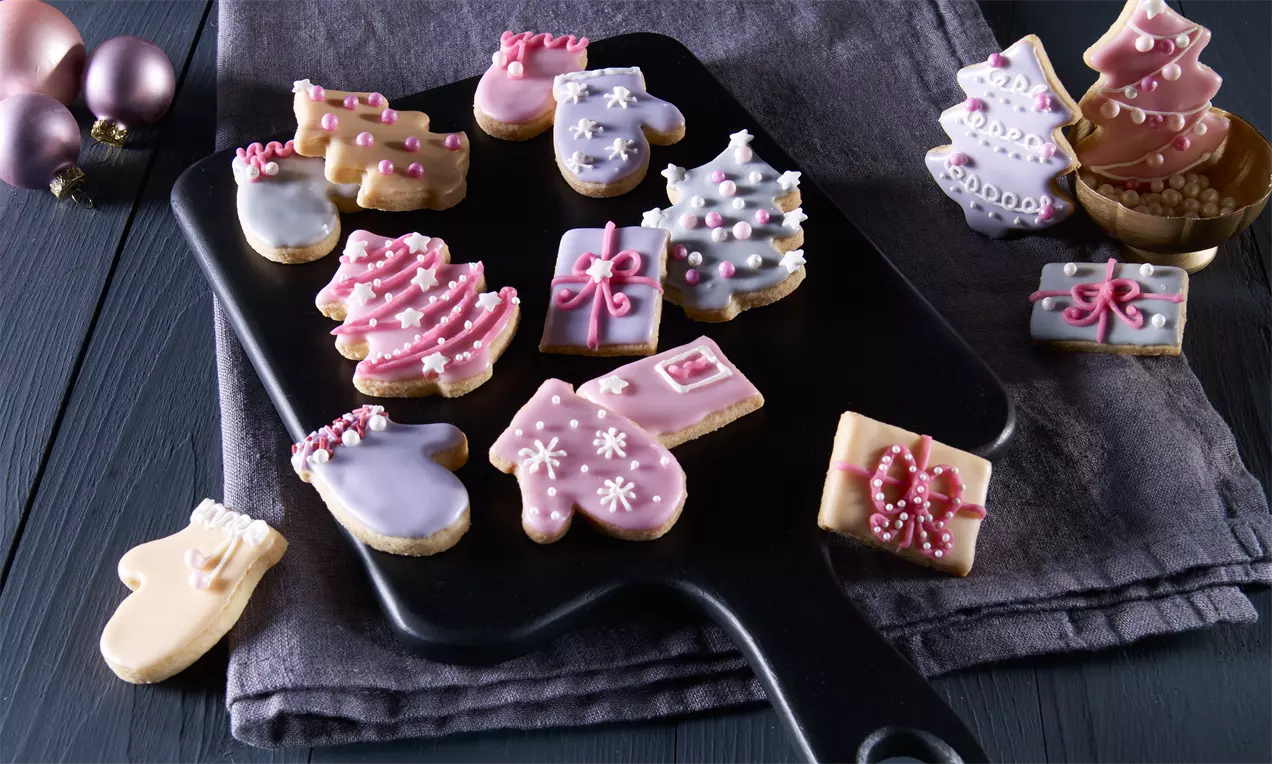 Zitronenplätzchen in weihnachtlichen Formen mit feiner Glasur und Dekor aus Perlen und Zuckerguss auf dunklem Brett mit Deko-Elementen drapiert